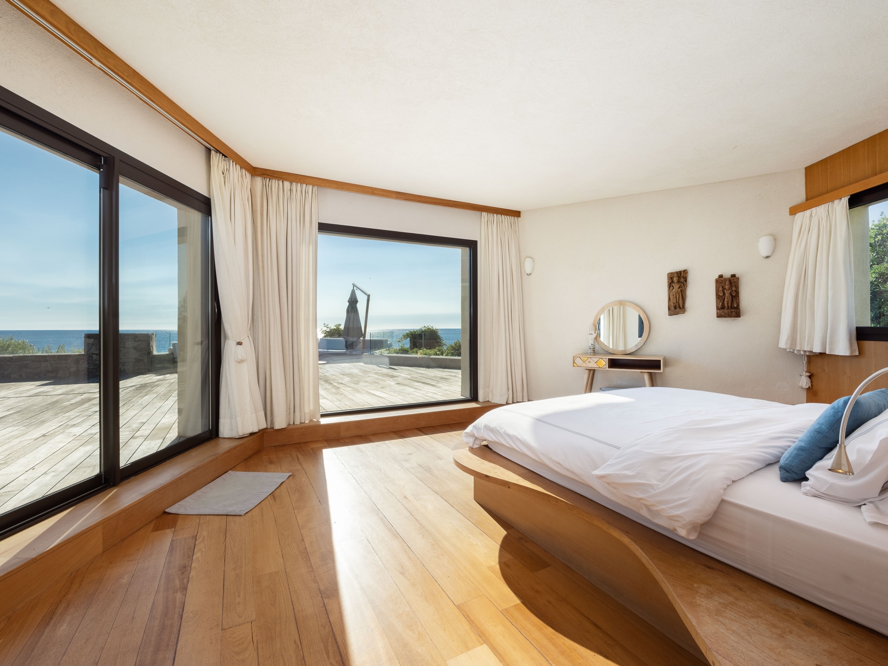 Chambre lumineuse avec larges baies vitrées, terrasse en bois et vue sur la mer Méditerranée